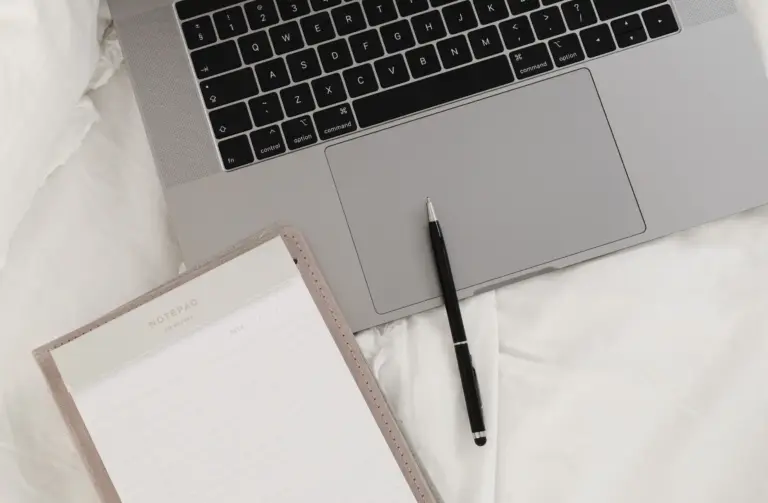 Laptop mit sichtbarer Tastatur, daneben ein schwarzer Stift und ein Notizblock auf weißer Decke
