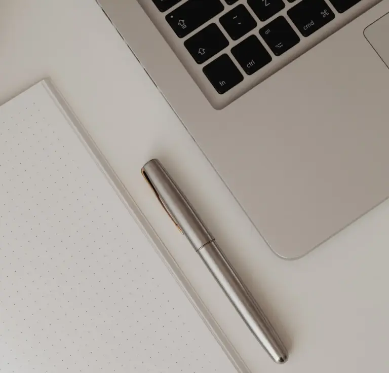 Ausschnitt einer Laptop-Tastatur neben einem Notizbuch mit Punktraster und einem silbernen Stift