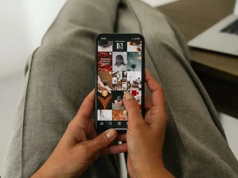Hand hält Smartphone mit Social-Media-Profil, das mehrere Beiträge vom Online-Business zeigt.